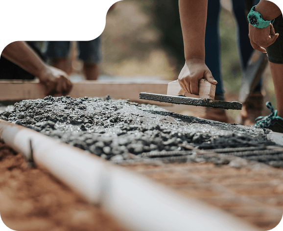Moderná obývačka s elegantnou rohovou sedačkou v béžovej farbe, zlatým konferenčným stolíkom a otvorenou kuchyňou v pozadí. Na pravej strane sa nachádza drevené schodisko so skleneným zábradlím vedúce na poschodie. Obrázok má kreatívne orezy so zaoblenými tvarmi.