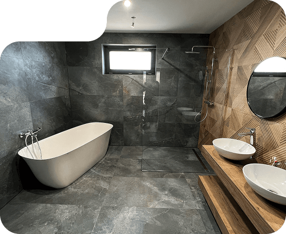 Moderná obývačka s elegantnou rohovou sedačkou v béžovej farbe, zlatým konferenčným stolíkom a otvorenou kuchyňou v pozadí. Na pravej strane sa nachádza drevené schodisko so skleneným zábradlím vedúce na poschodie. Obrázok má kreatívne orezy so zaoblenými tvarmi.