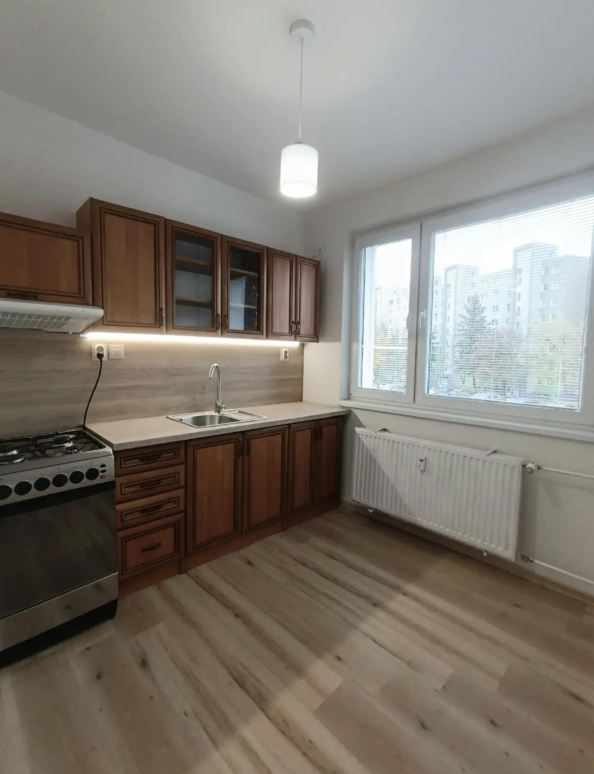 Štýlová tmavá kuchyňa s moderným osvetlením, zlatými akcentmi a elegantným jedálenským stolom.