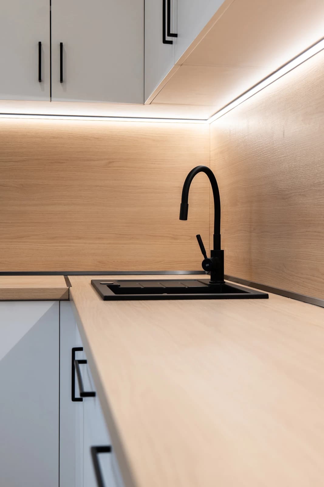 Štýlová tmavá kuchyňa s moderným osvetlením, zlatými akcentmi a elegantným jedálenským stolom.