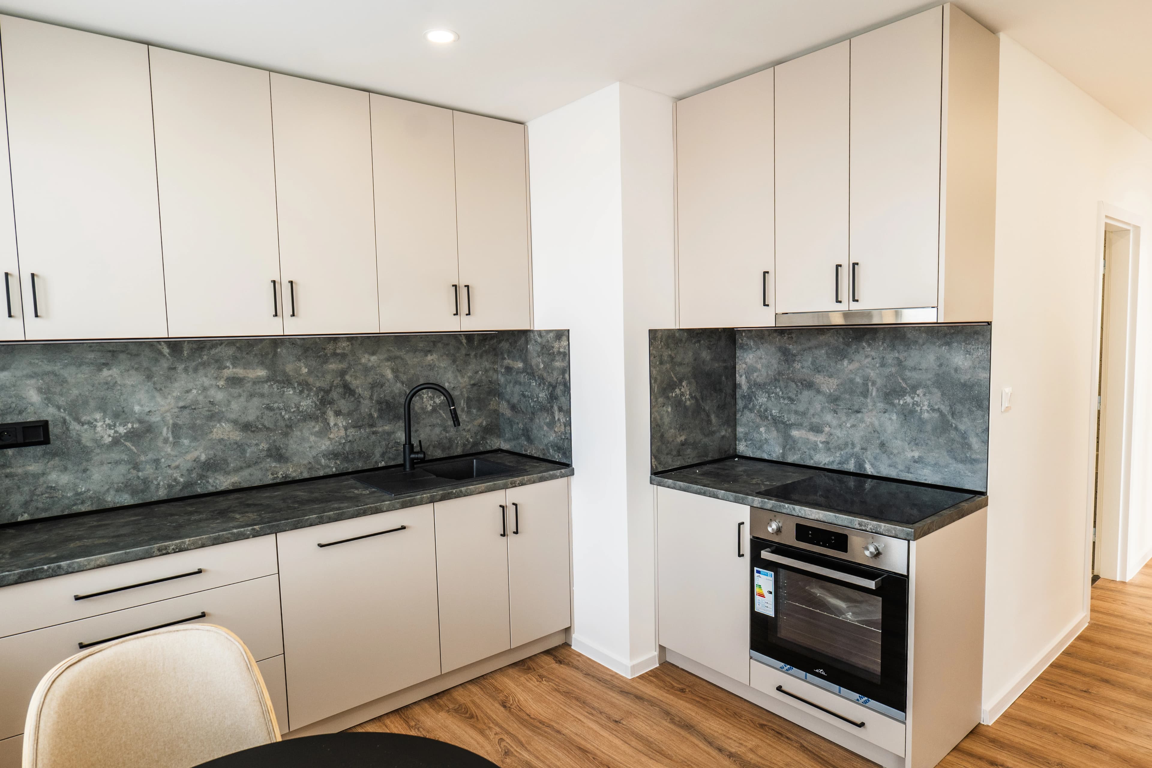 Štýlová tmavá kuchyňa s moderným osvetlením, zlatými akcentmi a elegantným jedálenským stolom.