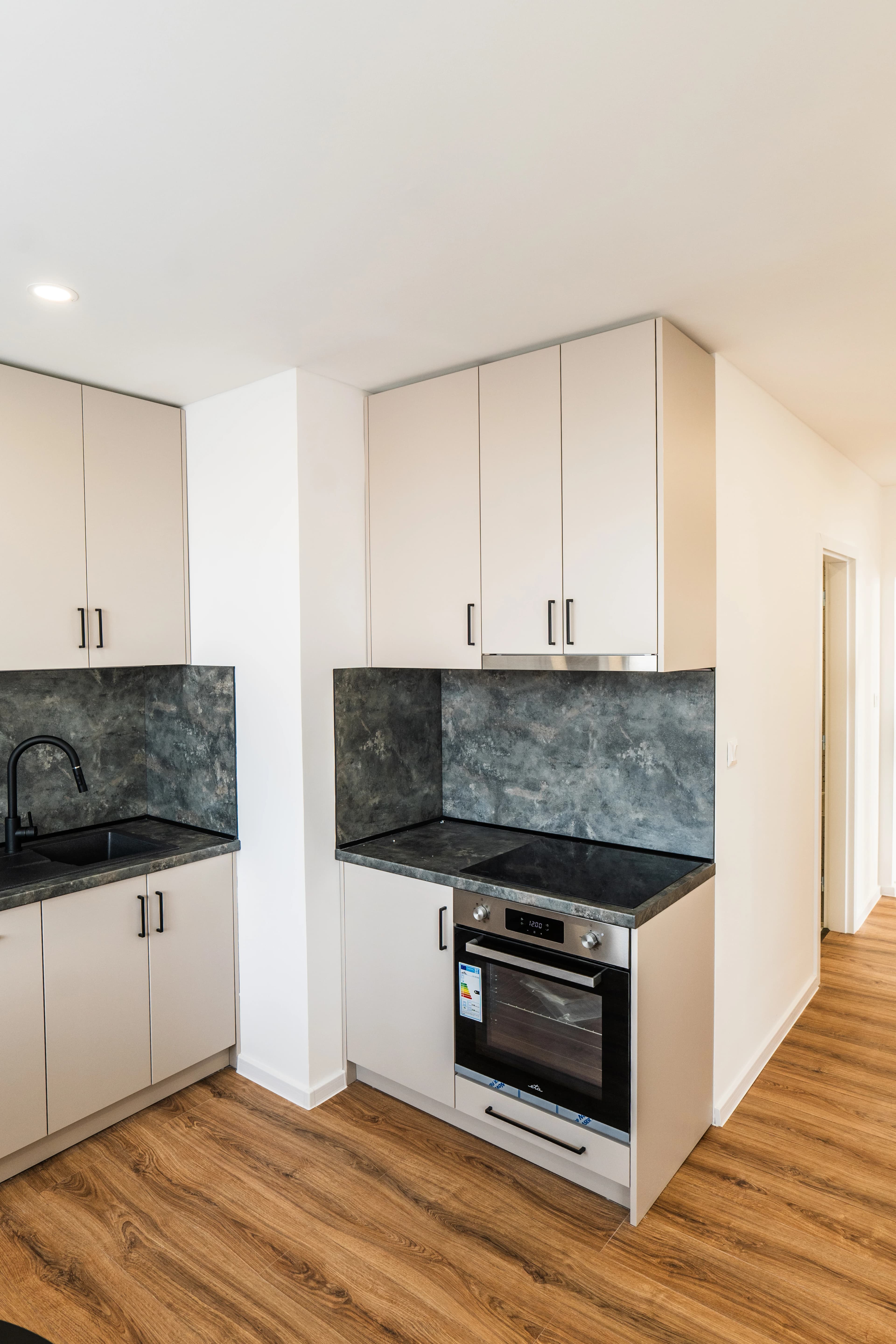 Štýlová tmavá kuchyňa s moderným osvetlením, zlatými akcentmi a elegantným jedálenským stolom.