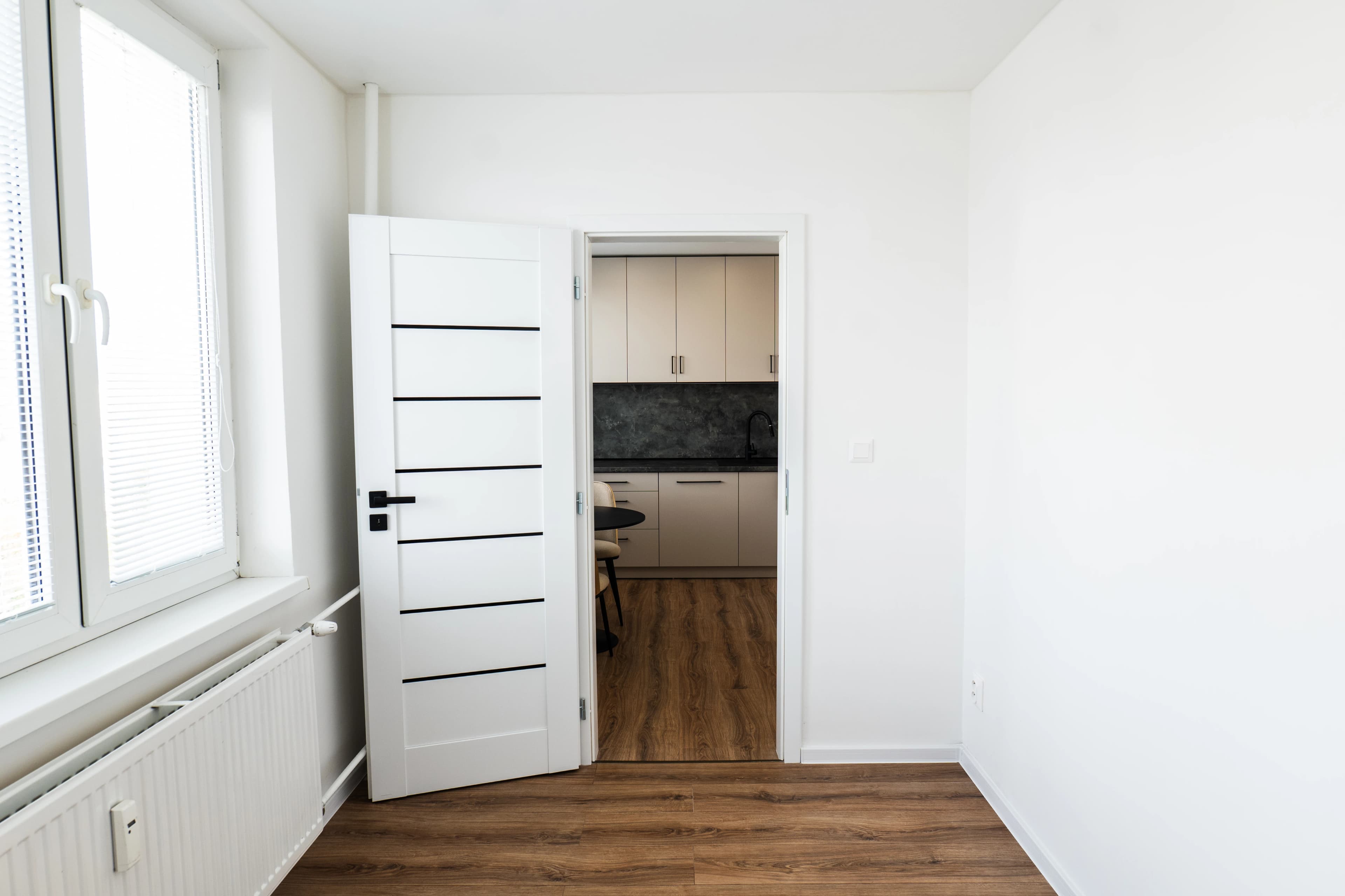 Štýlová tmavá kuchyňa s moderným osvetlením, zlatými akcentmi a elegantným jedálenským stolom.