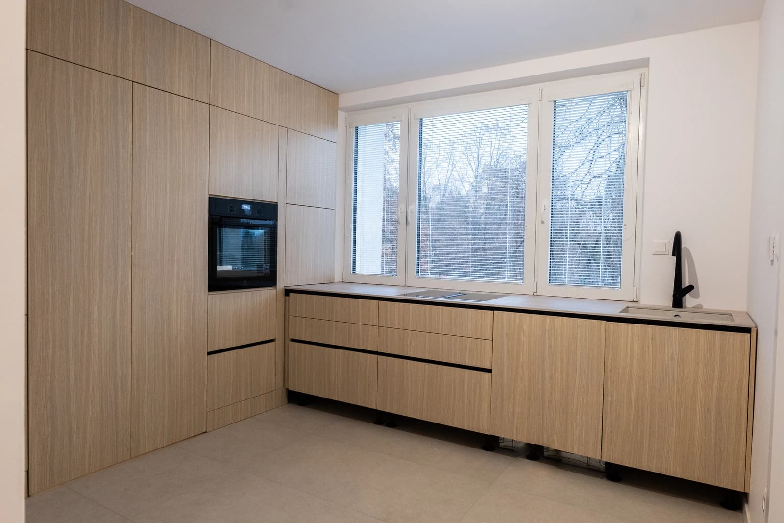 Štýlová tmavá kuchyňa s moderným osvetlením, zlatými akcentmi a elegantným jedálenským stolom.