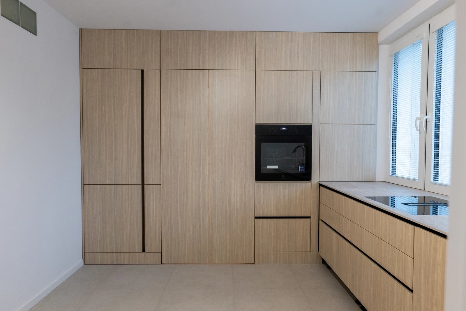 Štýlová tmavá kuchyňa s moderným osvetlením, zlatými akcentmi a elegantným jedálenským stolom.